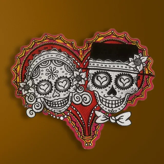Two decorated white skulls with heart-shaped eyes inside a red heart, with flowers, a black hat and a white bow tie